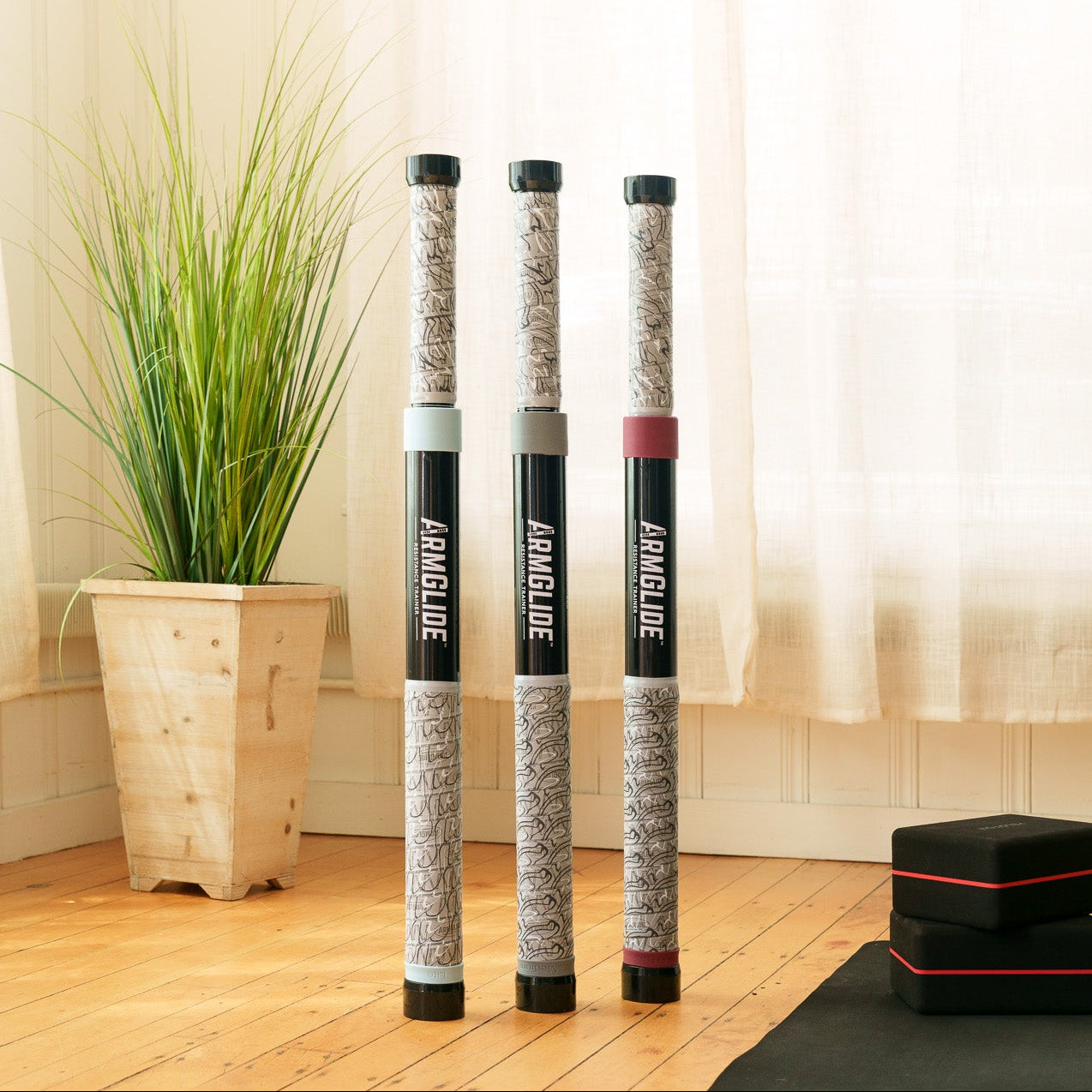 Three cylindrical products on a black mat with a plant and white curtains in the background